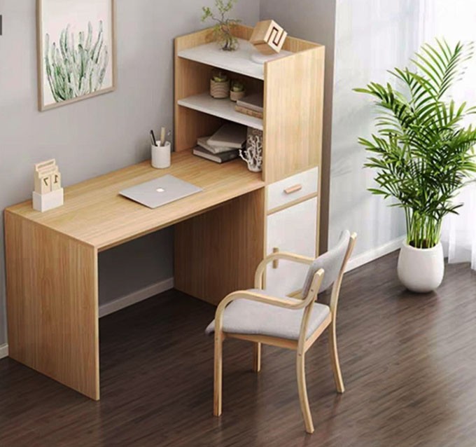 Người phụ nữ đang làm việc tại bàn làm việc gỗ, bên cạnh có cây xanh và cửa sổ lớn